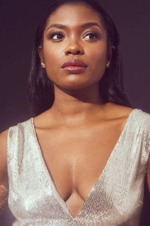 Portrait of a black woman in her 20s wearing a sparkling silver v-neck dress against a dark neutral studio background.