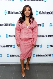 A smiling woman wearing a pink patterned skirt suit standing in front of a SiriusXM branded backdrop.