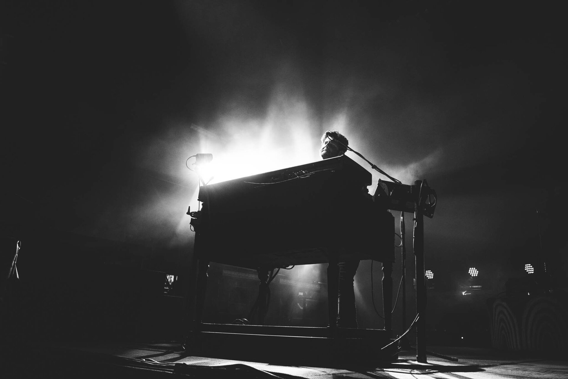 Monochrome shot of a musician playing a keyboard on stage, with a spotlight creating a dramatic and atmospheric setting.