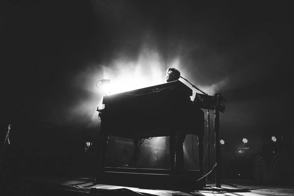 Monochrome shot of a musician playing a keyboard on stage, with a spotlight creating a dramatic and atmospheric setting.