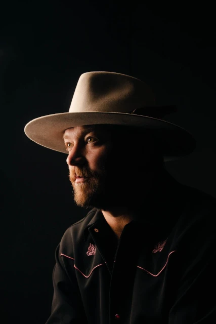 Headshot of a man with a beard wearing a cowboy hat and a western shirt against a black background, showcasing portrait lighting.