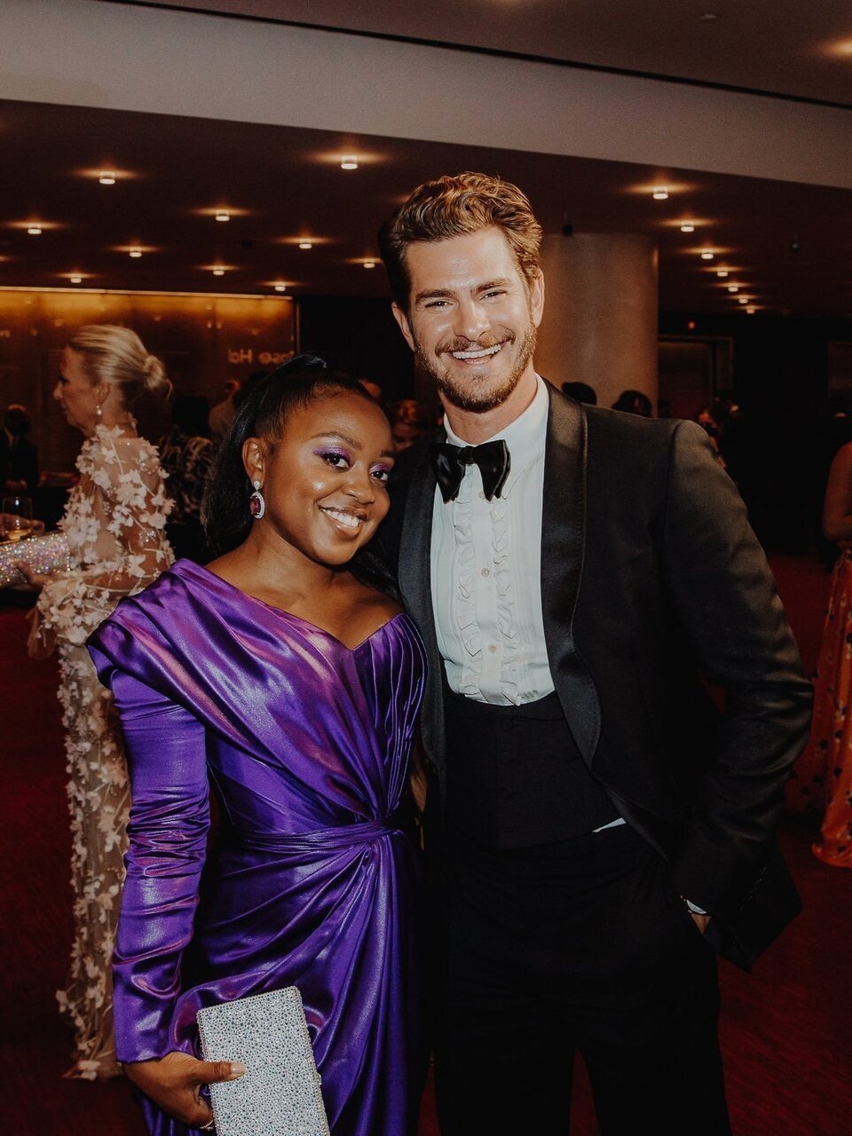 Andrew Garfield and Quinta Brunson pose together on a red carpet. Garfield wears a black tuxedo; Brunson a draped purple gown.