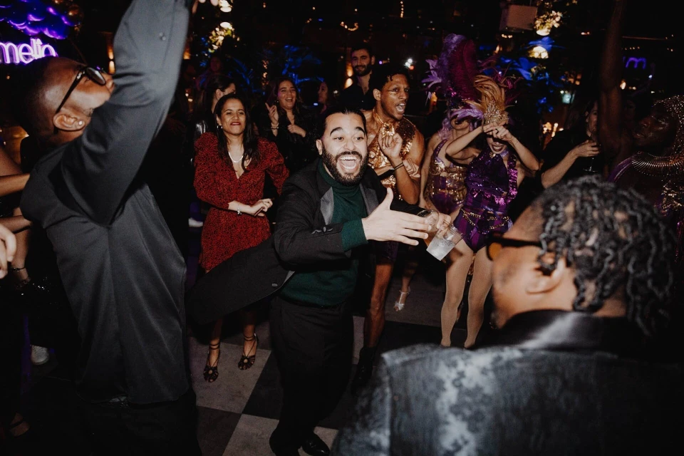 Enthusiastic crowd of people dancing at an indoor event with low lighting, featuring a diverse group and vibrant nightlife scene.