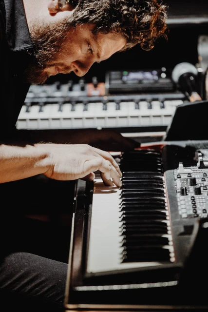 Man playing a black and white keyboard in a dark room, close up, with his hands and curly hair visible in the close shot.