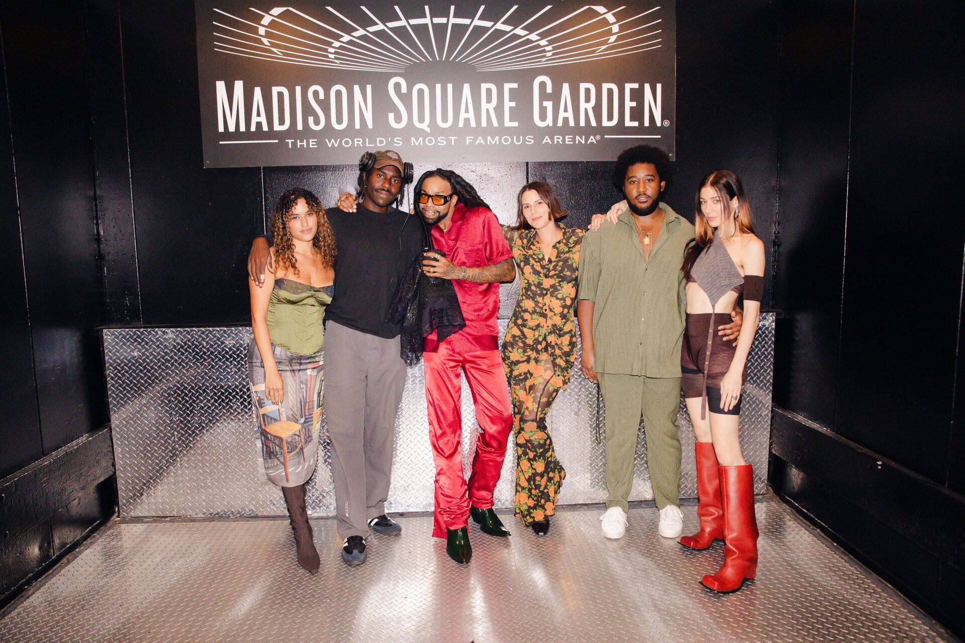 Group of six adults pose in front of Madison Square Garden sign, showcasing fashion-forward outfits with a mix of colors and styles.