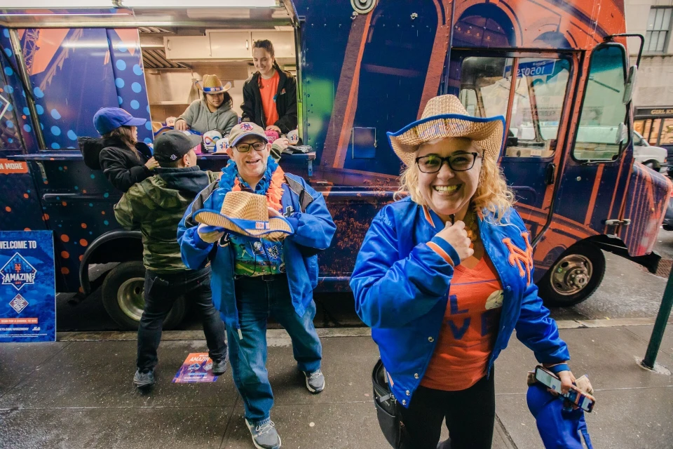 Happy adults wearing team apparel stand by a branded food truck on a city street, smiling at the camera, showcasing team spirit and urban vibes.