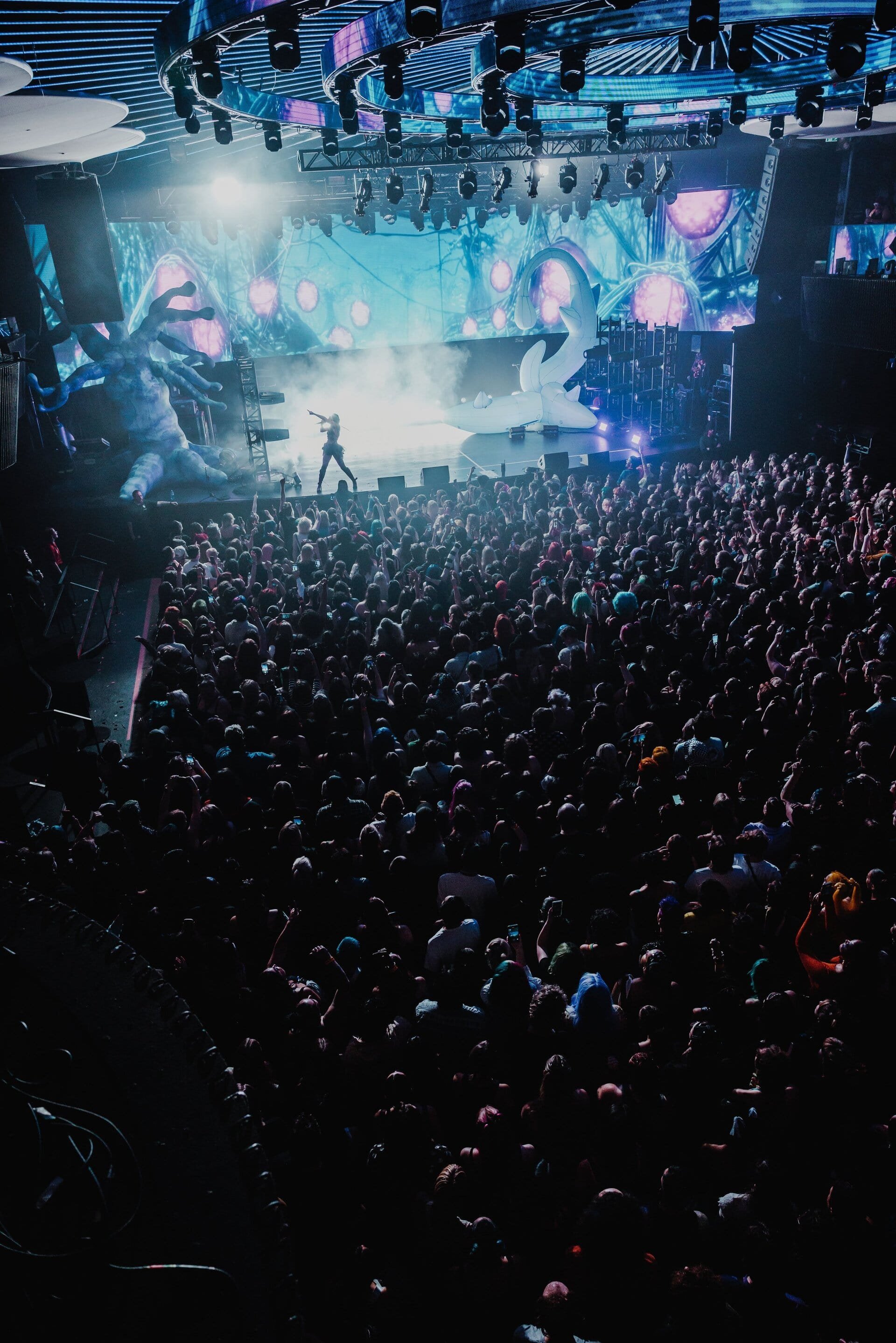 Concert performance shot with a crowd of people facing the stage with lights and an LED screen in the background; shot from an elevated angle.