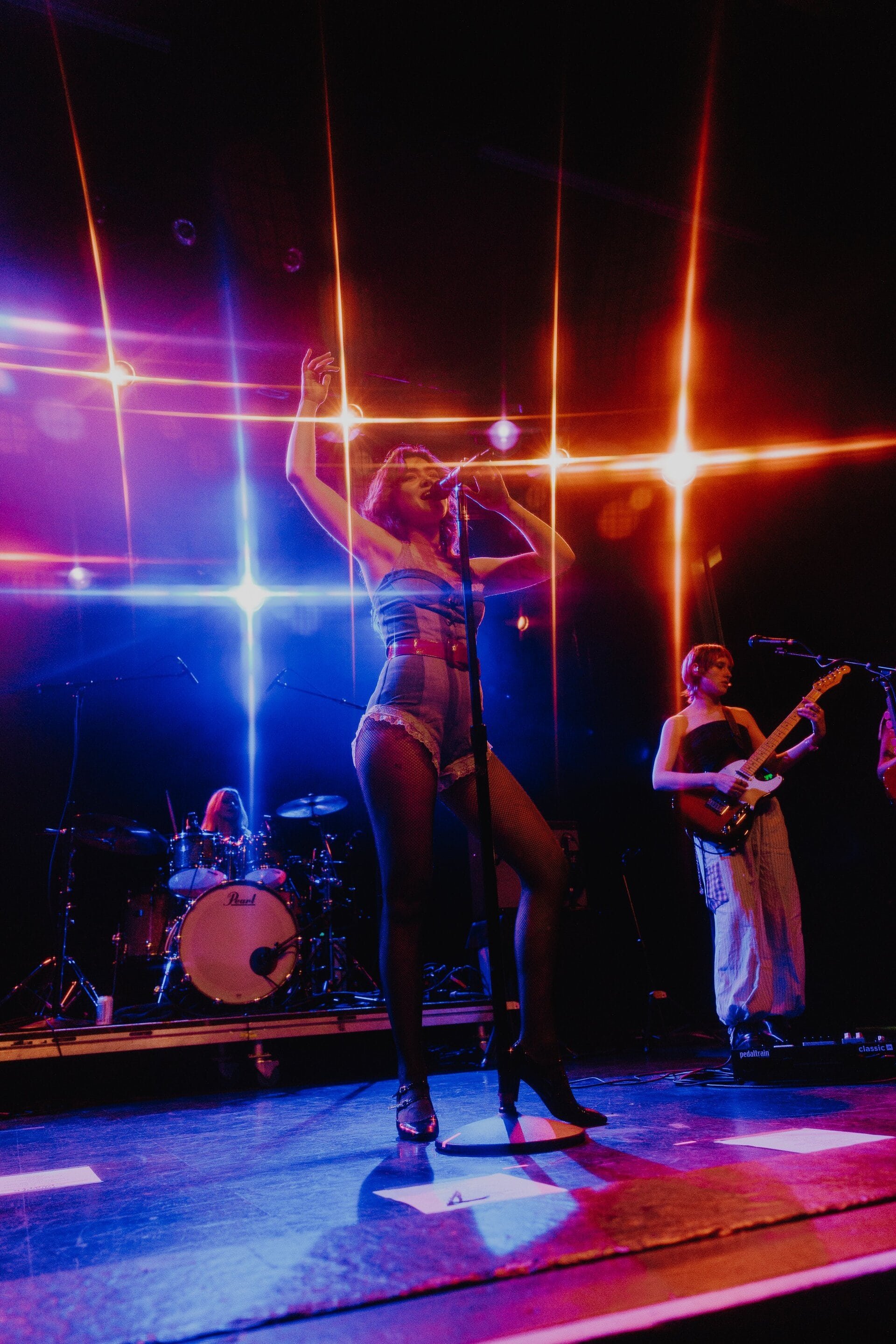 Singer performs on stage with band; dramatic lighting highlights her outfit and the musical performance.