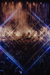 Concert stage framed by diamond neon lights with an audience silhouette, photographed by Maggie Friedman