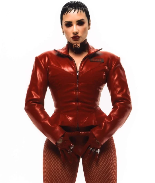 Adult female with short dark hair poses indoors wearing a form-fitting red jacket, gloves, and pants in a fashion or portrait style shot.