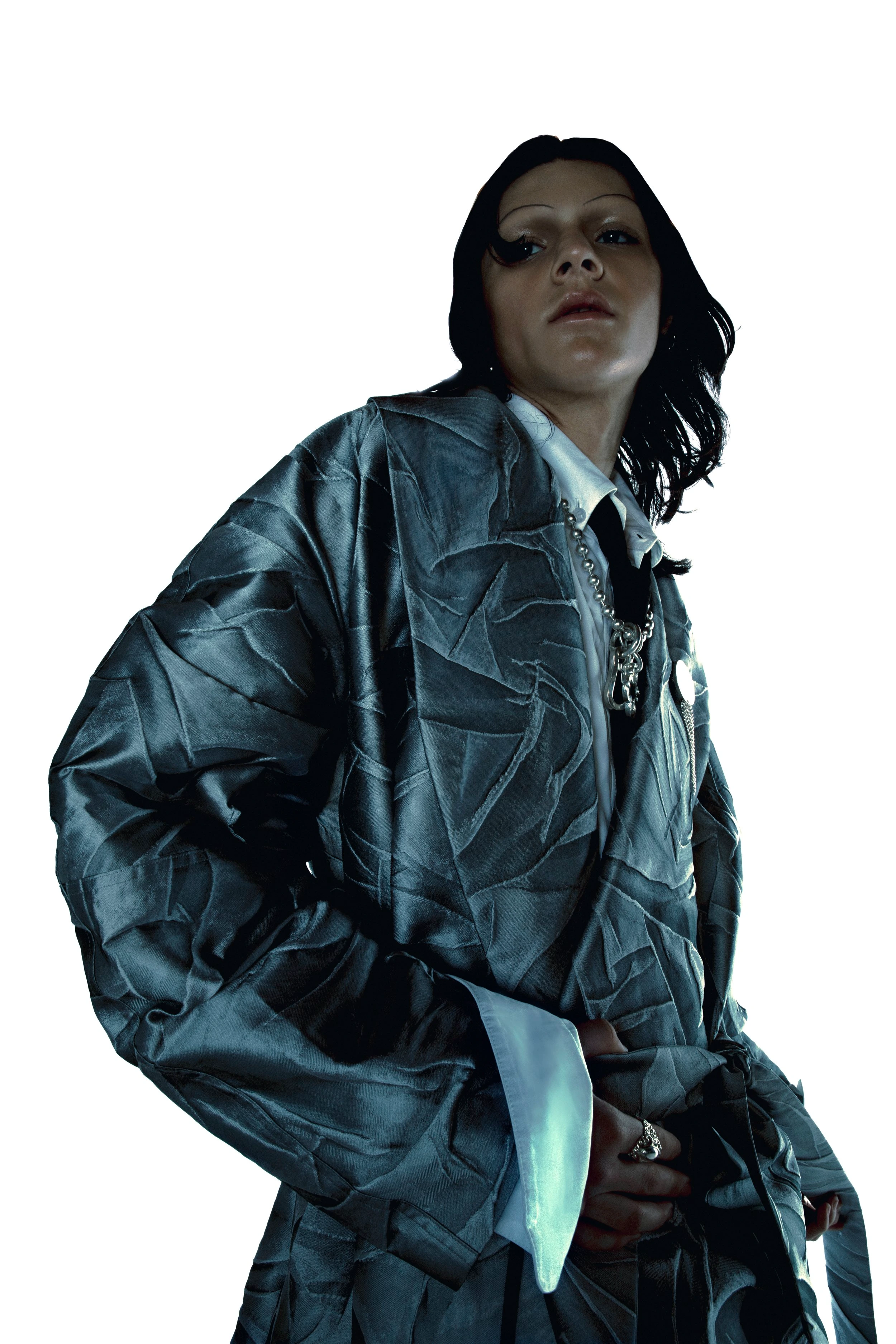 A woman in a textured robe looks at the camera. The model wears a collared shirt, jewelry, and a grey robe against a white backdrop.