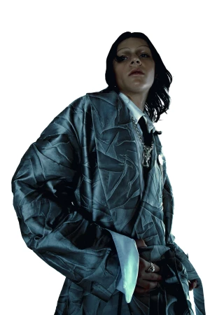 A woman in a textured robe looks at the camera. The model wears a collared shirt, jewelry, and a grey robe against a white backdrop.