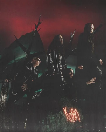 Band members of Korn in dark clothing stand against a dark forest backdrop with a red sky, illuminated by neon writing.