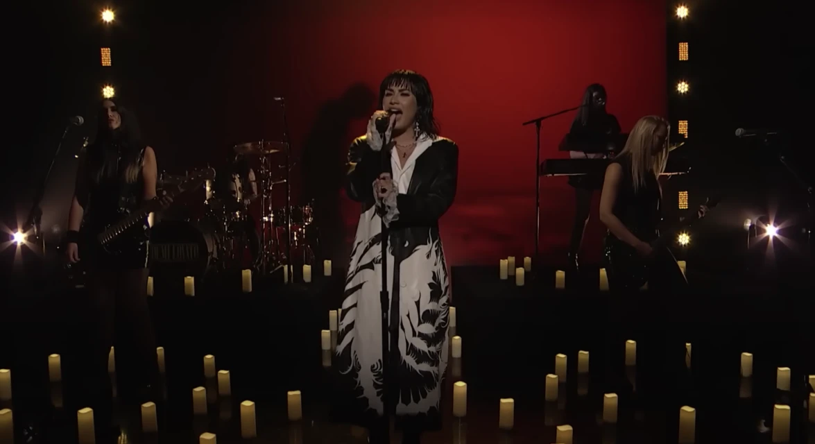 Female singer performing on stage with her band in dim lighting, surrounded by candles and a red backdrop during a live music event.