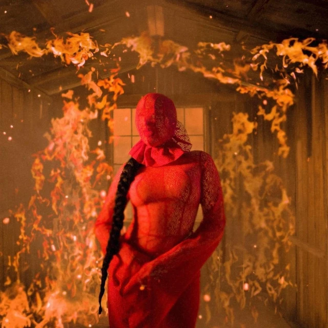 Abstract portrait of a red-clad person standing indoors with a lace face covering, contrasted by fire imagery and a dark background.
