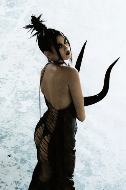 Portrait of a woman wearing a dark gown with long black gloves, posing in a studio against a blurred white background with textured effect.