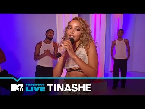 Tinashe performs live on MTV's Fresh Out stage, singing into a microphone, backed by two male dancers in a studio setting.