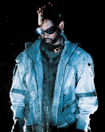 Man wearing dark sunglasses and a textured blue hooded jacket against a dark background, photographed by Maleeka Moss.