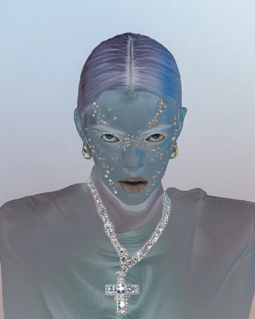Close-up portrait of a person with blue skin, jewelry, and light-colored eyes against a soft background. Conceptual fashion and beauty.