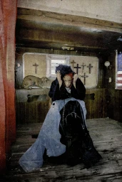 Person seated inside rustic wooden interior with taxidermy animal and crosses on wall, photographed by Maleeka Moss