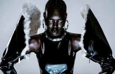 Portrait of a model in a black glossy top and dramatic fur-trimmed sleeves by Maleeka Moss