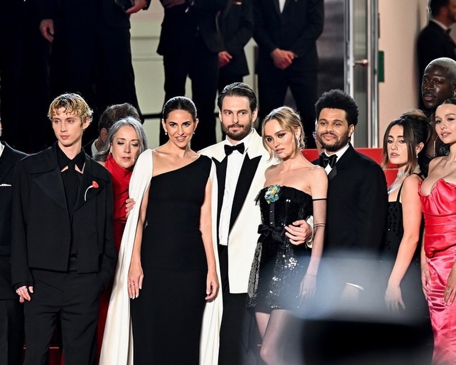 Cannes Film Festival red carpet scene with multiple celebrities posing in formal attire, captured in a medium shot, with black and red color palette.