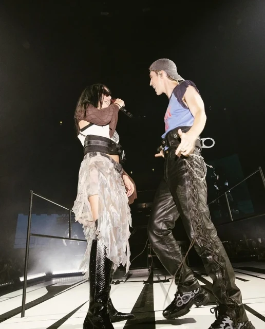 Two musicians, a male and female, perform on stage during a concert, captured from a low angle with stage lighting.