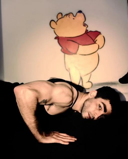 Adult male doing push ups, looking into camera with Disney character Winnie the Pooh illustration in the background, in a fitness setting.