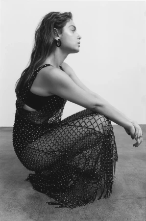 Profile view of a woman crouching in a black mesh beaded dress styled by Marco Milani against a plain studio background.