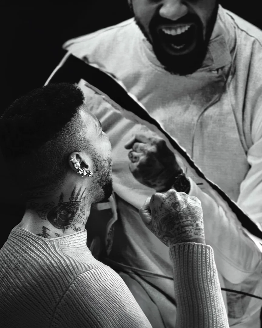 Monochromatic portrait of two adult males facing each other, one shouting with tattoos and an earring, the other in a ribbed sweater.