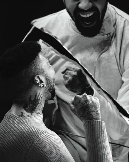 Monochromatic portrait of two adult males facing each other, one shouting with tattoos and an earring, the other in a ribbed sweater.