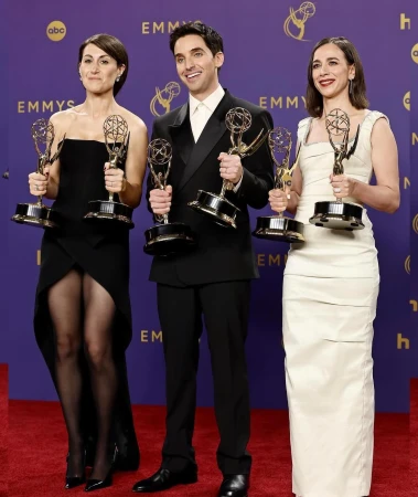 Three smiling people in formal attire, holding Emmy awards, stand in front of a purple backdrop at an entertainment event.