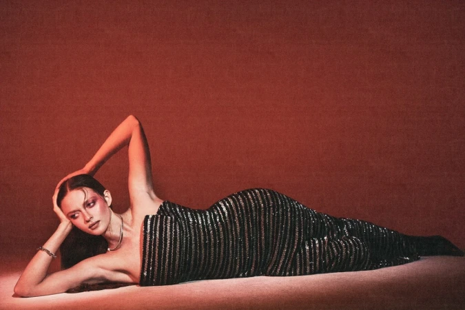 A woman in a sequined strapless dress lying on a red studio floor, styled by Maren Taylor.