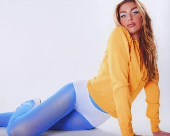 Model in yellow cardigan and blue tights posing against a white background styled by Maren Taylor