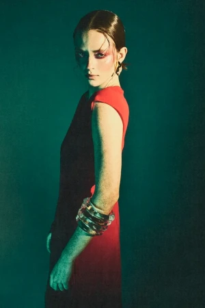 Model in red and black sleeveless dress with stacked bracelets against a teal background, styled by Maren Taylor.