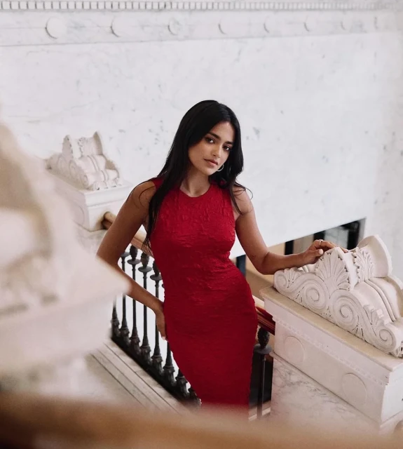 Elegant woman in a red dress poses on a marble staircase, showcasing classic style and sophistication in a luxurious setting.