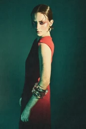 A model with slicked-back hair and bold pink eyeshadow wears a color-blocked red and dark dress with chunky translucent bangles.