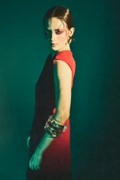 Model in red and black sleeveless dress with stacked bracelets against a teal background, styled by Maren Taylor.