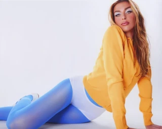 Model in yellow cardigan and blue tights posing against a white background styled by Maren Taylor