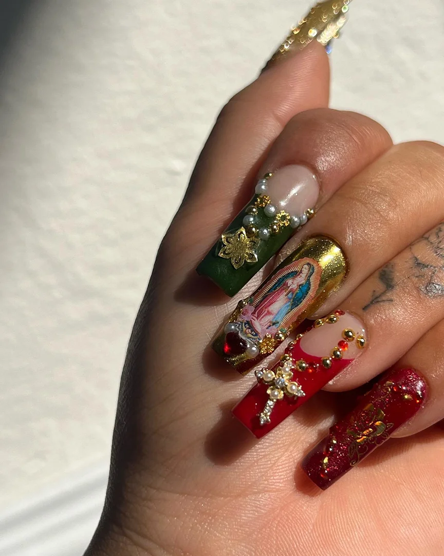 Close-up of hand showcasing long coffin-shaped nails with elaborate Christmas-themed nail art featuring religious and festive embellishments.