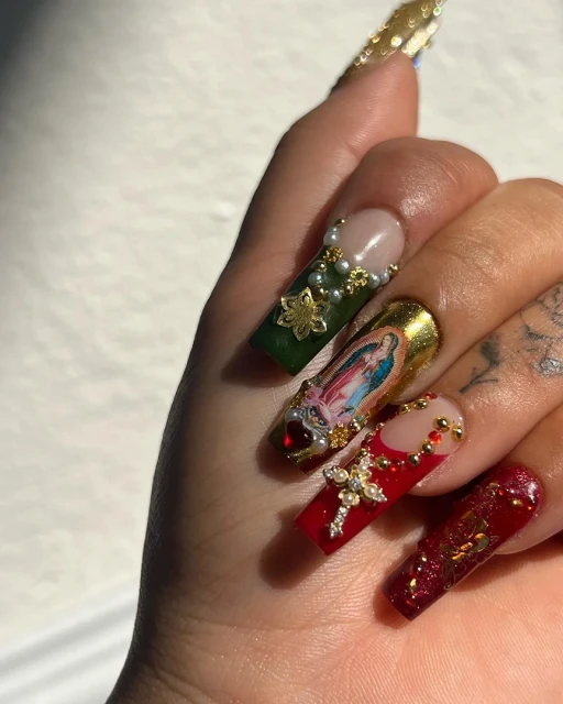 Close-up of hand showcasing long coffin-shaped nails with elaborate Christmas-themed nail art featuring religious and festive embellishments.