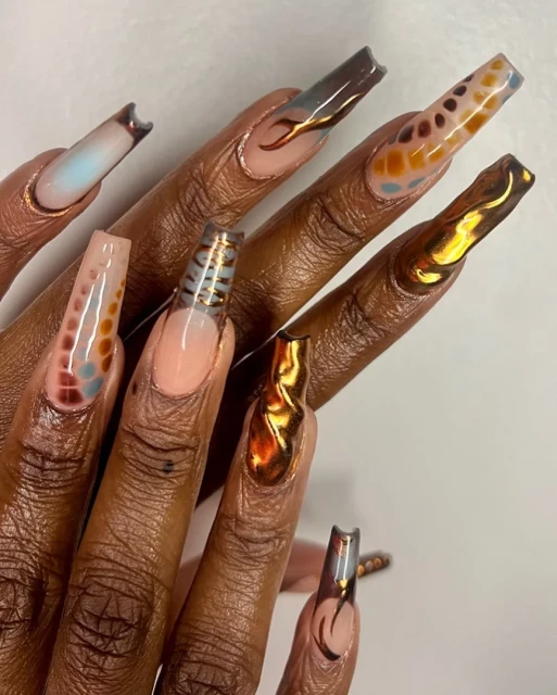 Close-up of a hand with extra-long coffin-shaped nail extensions showcasing various textures, colours, and patterns in a studio setting.