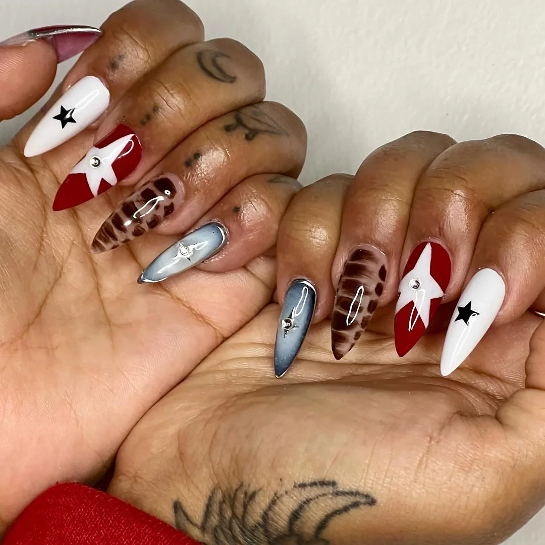 Close-up of a woman's hands displaying long, decorated nails with stars and animal print designs, set against a plain backdrop.