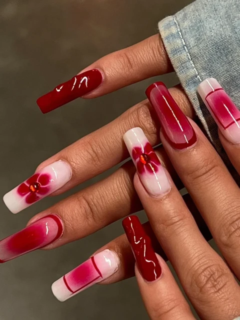 Close-up of a woman's hand showcasing a red and white square-shaped nail design, featuring solid red nails and floral accents.
