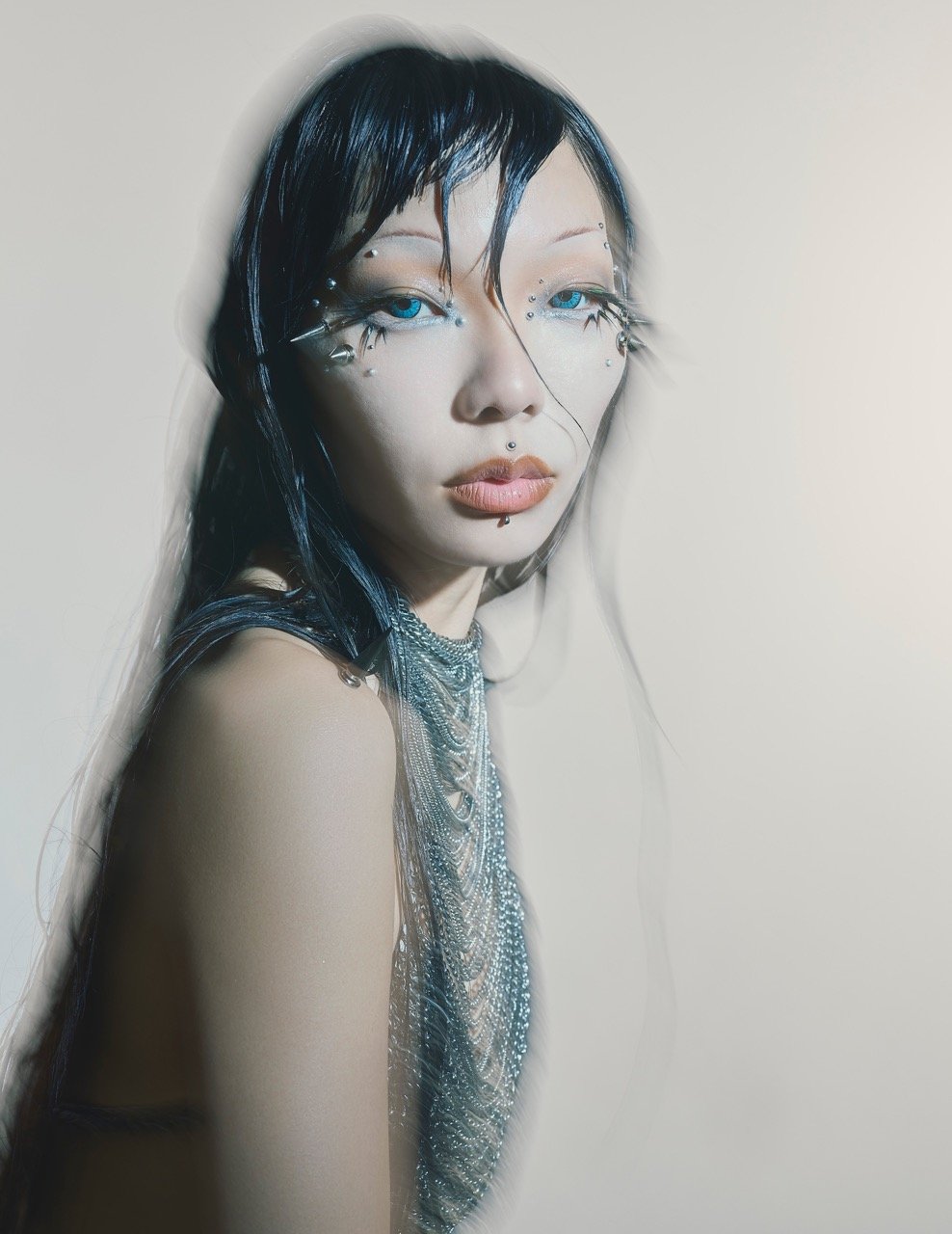 Close-up portrait of a woman with stylized makeup and embellished jewelry, against a soft background in a studio setting with diffused light.