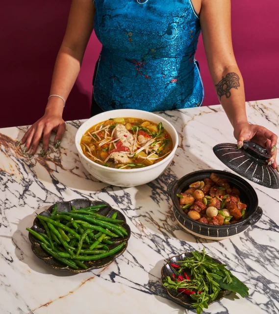 Overhead shot of a person serving a traditional Asian meal on a marble table with bean sprouts, chillies, and green beans.
