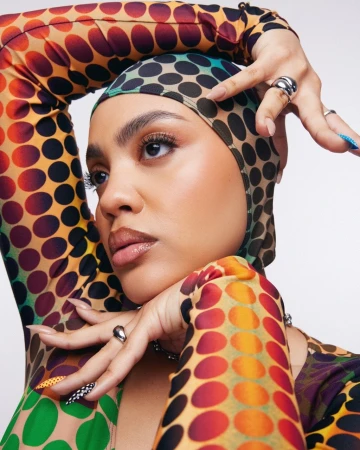 Close-up portrait of a woman wearing a colorful polka-dot top and matching head covering with intricate nail art by Marielle Co.