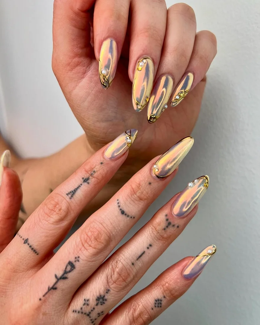 Close-up of woman's hands showcasing iridescent, almond-shaped nail art with gold wire and pearl accents, set against a neutral backdrop.