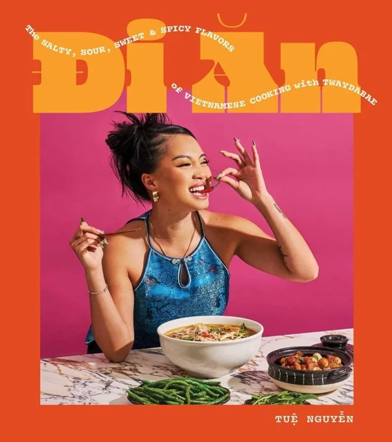Book cover featuring a woman about to eat a red pepper, with a bowl of pho and greens on a marble table against a pink backdrop.