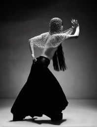 Model with long dark hair wearing a beaded chainmail headpiece and dark skirt posing against a grey studio backdrop